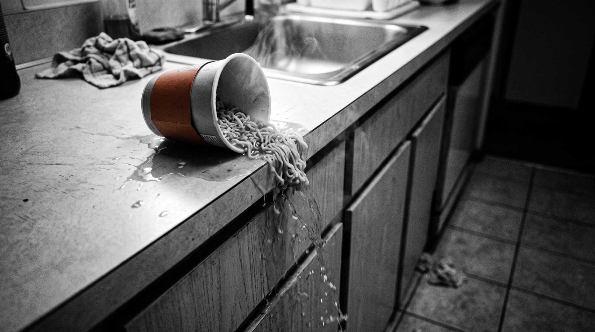 A tipped instant soup cup spilling hot broth off a counter (photo illustration)