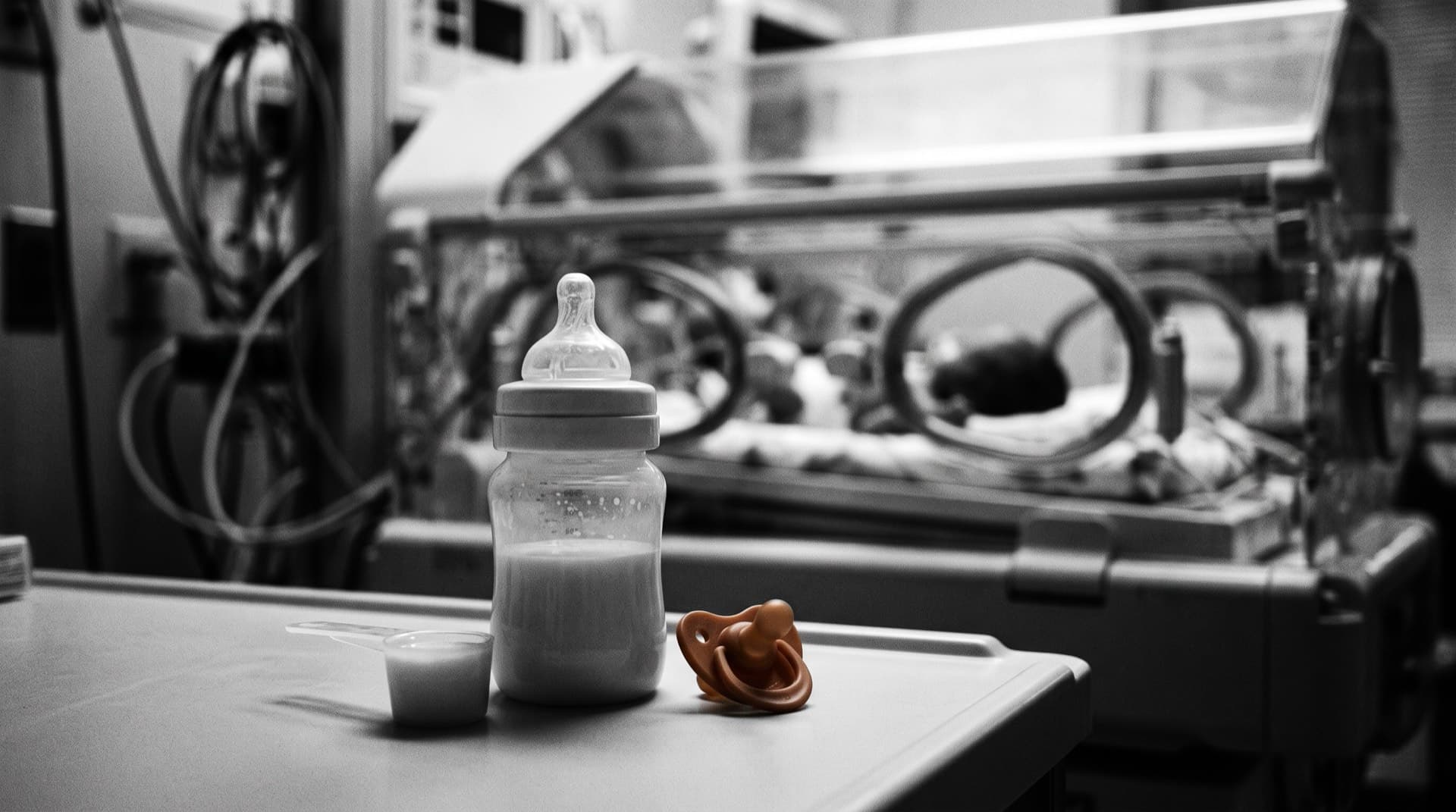 A formula bottle and scoop with a blurred incubator behind (photo illustration)